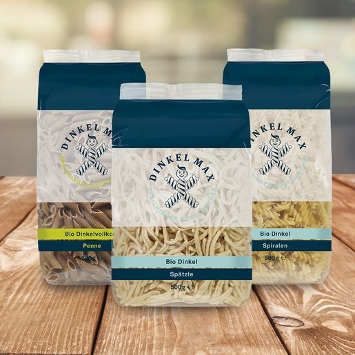 Drei Packungen Bio Dinkel Nudeln der Marke DINKEL MAX auf einem Holztisch Drei Packungen Bio Dinkel Nudeln der Marke DINKEL MAX auf einem Holztisch